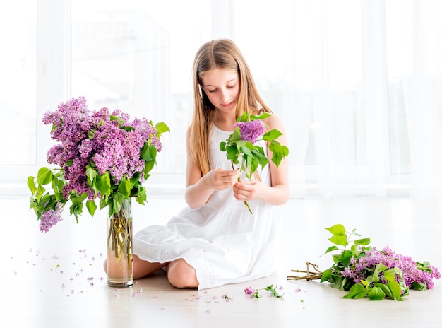 Fille avec bouquet de fleurs lilas assis sur le sol