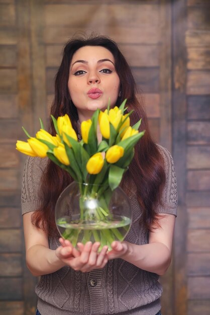 Fille avec un bouquet de tulipes jaunes Fille avec un cadeau de fleurs dans un vase Un cadeau pour les filles en vacances féminines avec des tulipes jaunes sur le sol