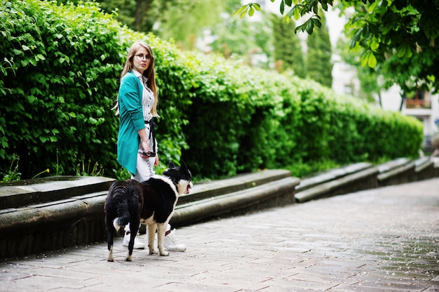 Fille branchée à lunettes et déchiré jeans avec chien laika (husky) russo-européen sur une laisse, contre rue de la ville