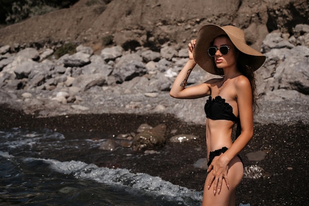 Fille bronzée sexy dans un chapeau de paille posant au bord de la mer