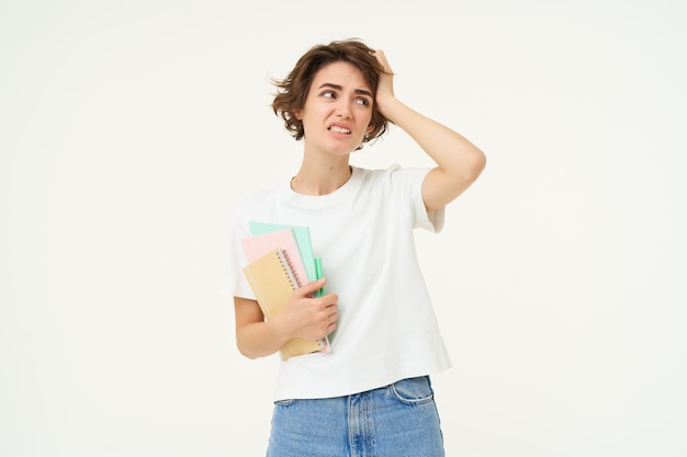 Une fille brune a l'air d'une étudiante en difficulté avec des problèmes et tient des cahiers et des devoirs avec un visage confus