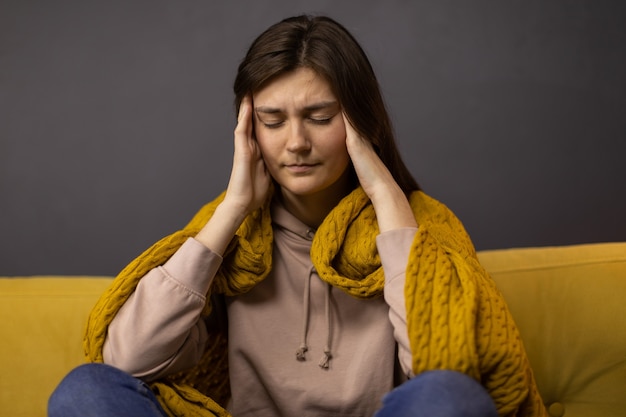 Fille brune attrapant sa tête du mal de tête avec une expression de douleur et une couverture sur ses épaules