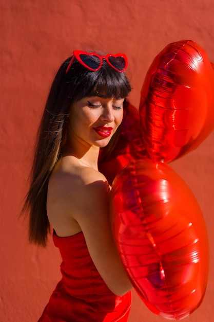 Fille brune caucasienne avec des ballons coeur sur fond rouge Saint Valentin