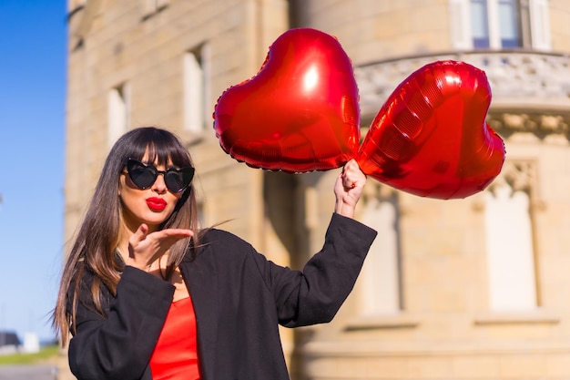 Fille brune caucasienne avec des ballons coeur sur la Saint-Valentin lunettes de soleil et robe rouge