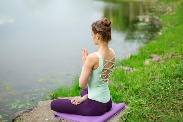 Fille brune caucasienne mince, faire du yoga en été sur une pelouse verte au bord de la rivière