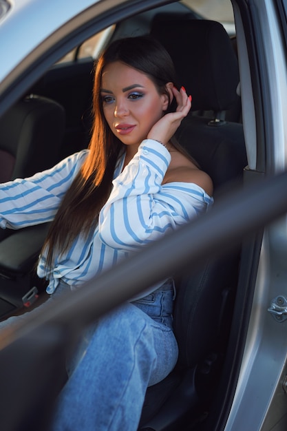 fille brune dans une chemise rayée et un jean au volant d'une voiture