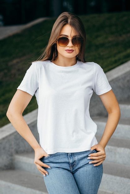 Fille brune élégante portant un t-shirt blanc et des lunettes posant contre le style de vêtements urbains de la rue