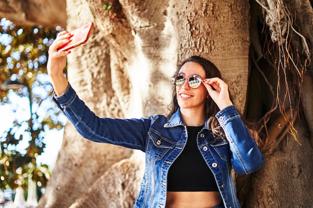 Fille brune avec des lunettes de soleil faisant un selfie avec le téléphone portable