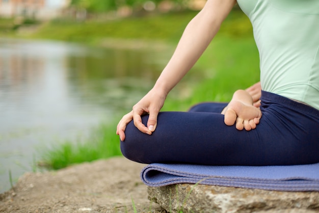 Fille brune mince, faire du yoga en été sur une pelouse verte au bord du lac