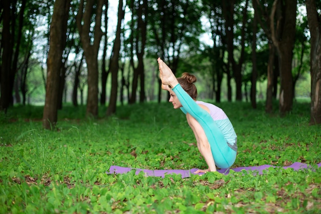 Fille brune mince fait du sport et effectue des poses de yoga belles et sophistiquées dans un parc d'été