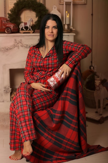 une fille brune en pyjama est assise sur une chaise près de la cheminée avec une boîte-cadeau dans les mains