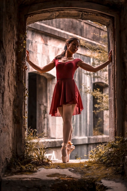 Fille brune en robe rouge danse ballet sur la pointe des pieds dansant dans une belle fenêtre