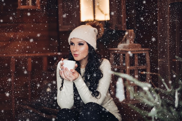 Fille brune romantique au chapeau buvant du cacao chaud sous la neige