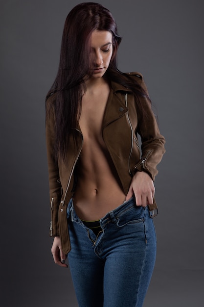 Fille brune sexy aux cheveux longs chic redresse un jean déboutonné