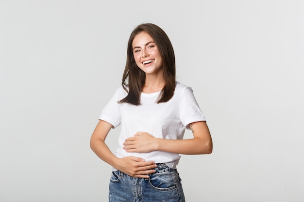 Fille brune souriante satisfaite se frottant le ventre après avoir mangé de la nourriture délicieuse.