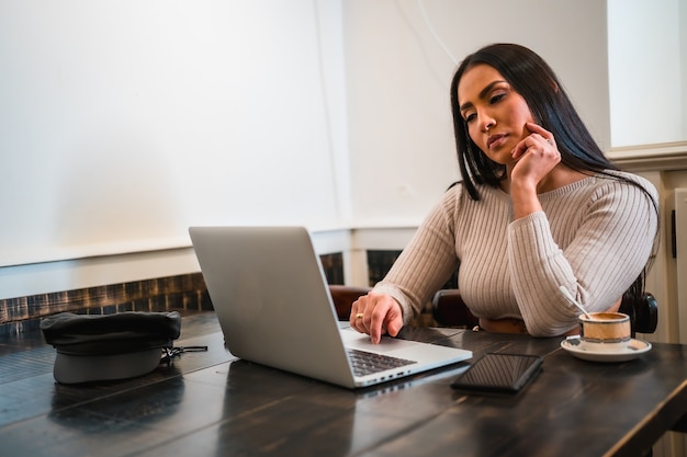 Fille brune télétravaillant dans un café avec un ordinateur portable avec un café