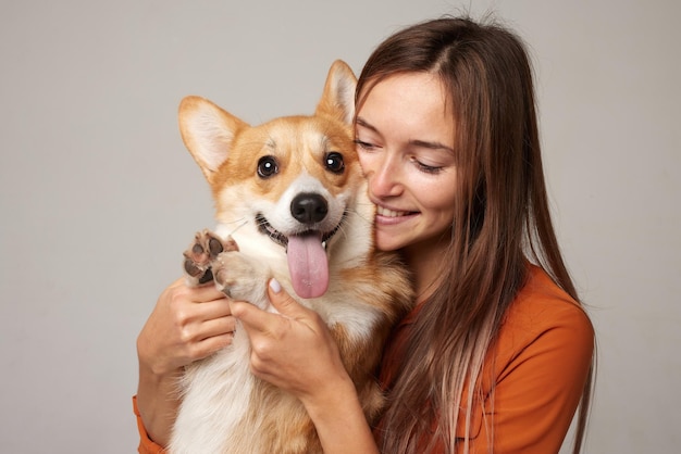 une fille brune tient et embrasse un chien corgi rouge sur un fond clair le concept d'amour pour les animaux