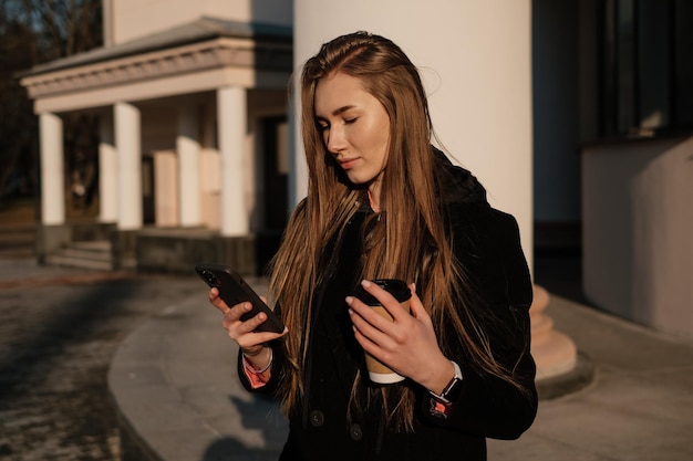 Fille buvant du café dans la rue et envoyant un message au téléphone