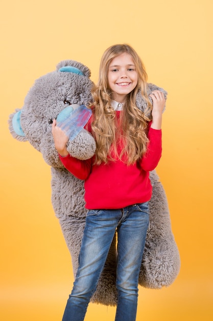 Fille câlin gros ours en peluche sur fond orange