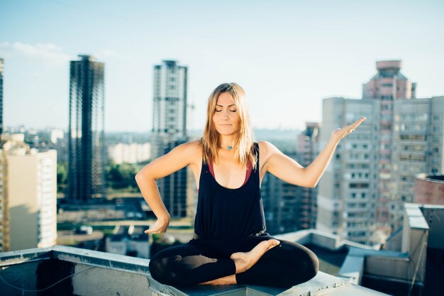 Fille calme assis sur le toit en position du lotus avec les yeux fermés