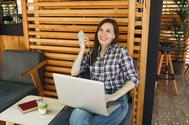 Fille calme dans la rue en plein air café d'été café en bois assis avec sur ordinateur portable moderne, téléphone portable