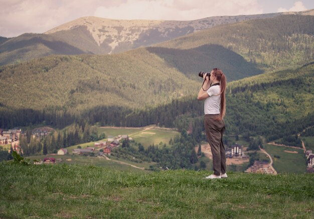 Fille avec caméra se dresse sur une colline et photographier une montagne.