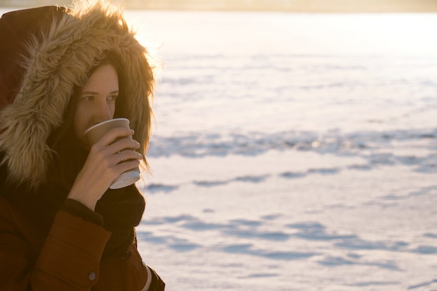 Fille à capuche boit du café chaud le jour de l'hiver