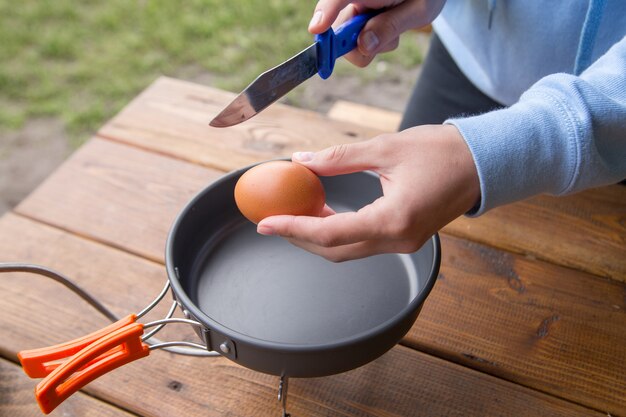 Fille casse un œuf pour cuisiner omlene sur un pique-nique au camping