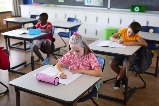 Fille caucasienne étudiant assise sur son bureau dans la classe à l'école