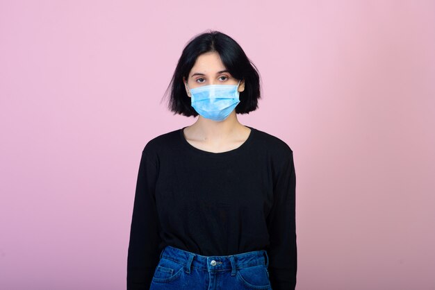 La fille caucasienne en masque protecteur de couleur bleue. Portrait tourné sur fond rose. concept de protection contre les virus et la pollution.