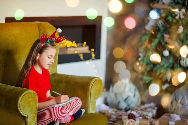 La fille caucasienne mignonne drôle de gaucher écrit une lettre au père Noël près de l'arbre de Noël