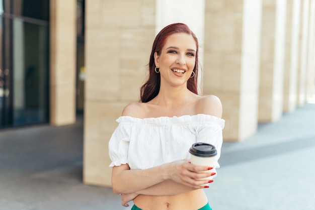 Fille caucasienne rousse souriante et tenant une tasse de café.