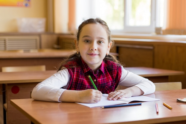 Fille caucasienne souriante assise au bureau dans la salle de classe et prête à étudier.