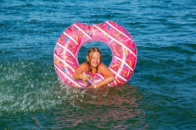 Une fille avec un cercle gonflable sous forme de beignet se baigne dans la mer