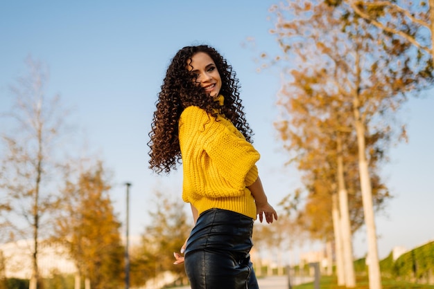 Fille en chandail jaune vif pose dans le parc d'automne