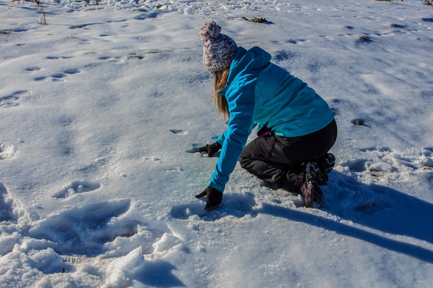 Fille avec chapeau attraper la neige du sol sur la montagne.