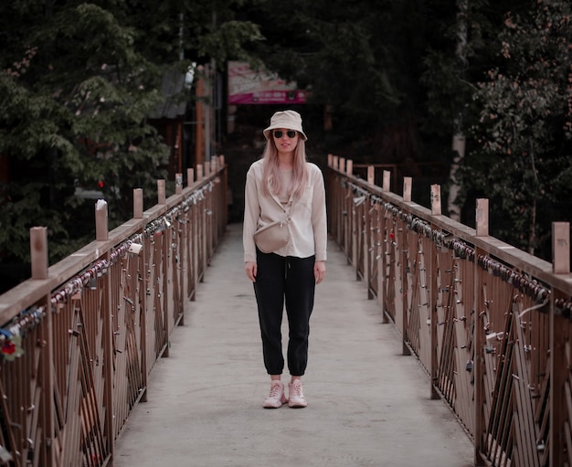 Une fille avec un chapeau beige et une chemise beige se tient au milieu du pont.