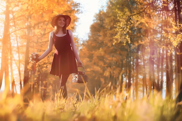 Une fille avec un chapeau lors d'une promenade dans le parc Une fille avec un panier se promène en automne Une fille marche le long de la route au coucher du soleilxA