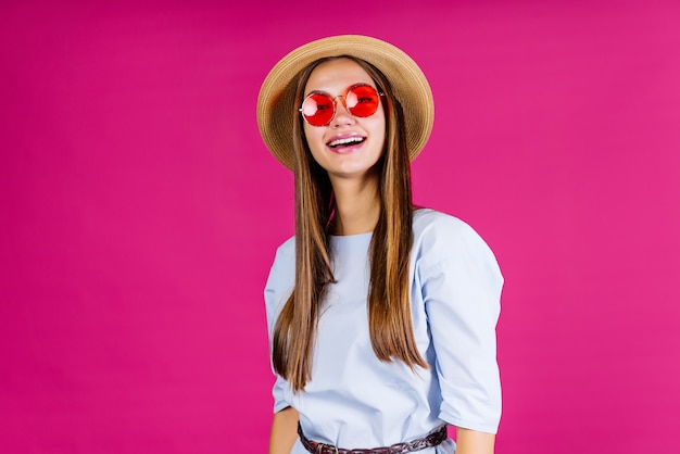 Une fille avec un chapeau et des lunettes s'exclame quelque chose. fond rose