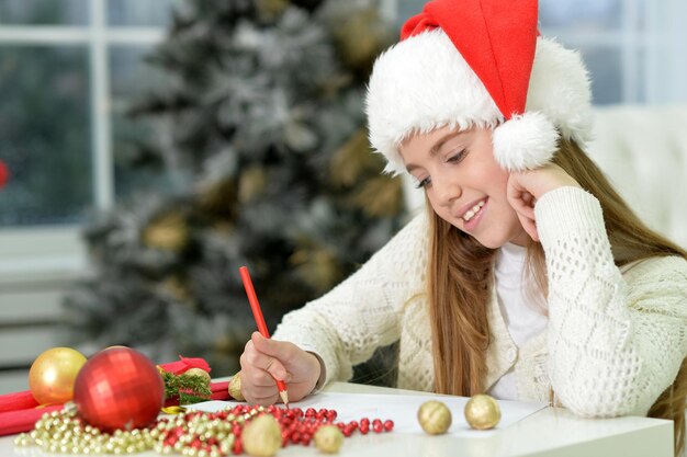 La fille avec le chapeau de Père Noël écrit une lettre à la maison.