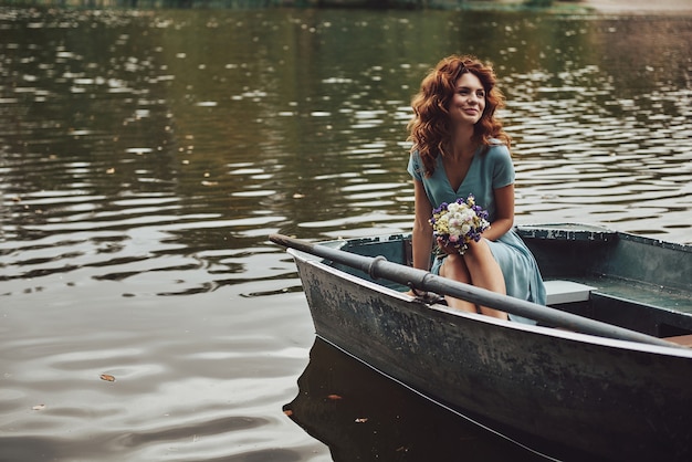 Fille charmante. Belle jeune femme en robe élégante en détournant les yeux et souriante assise dans le bateau