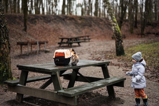 Fille avec chaton et chariot de cage en plastique de voyage en plein air au parc sur une table en bois