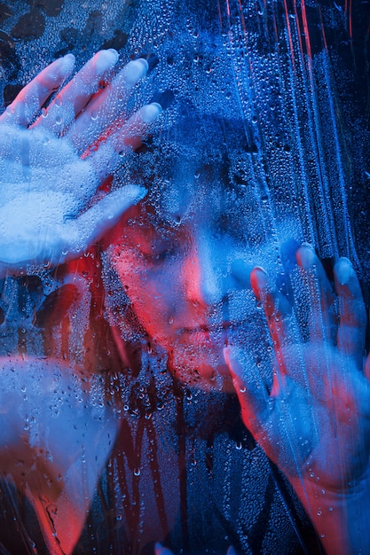 Fille chaude. Studio tourné en studio sombre avec néon. Portrait de la belle femme derrière une vitre humide