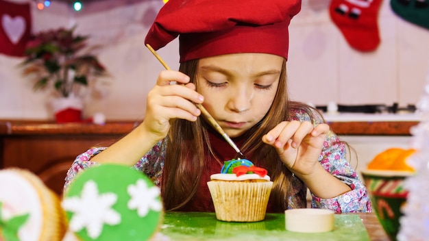 Une fille de chef gaie décorant un petit gâteau. Ambiance d'avant Noël