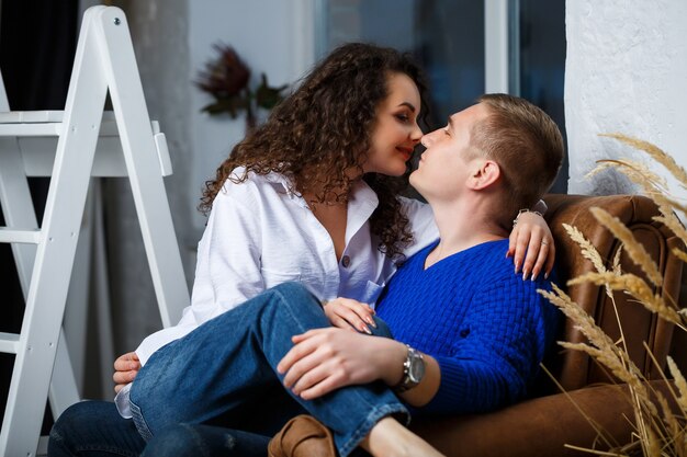 Une fille en chemise blanche et un gars en swirere bleu sont assis sur un fauteuil et s'embrassent, s'embrassent, tendent, amour