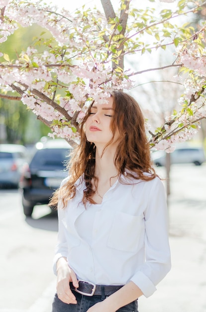 fille en chemise blanche se tient près de la sakura