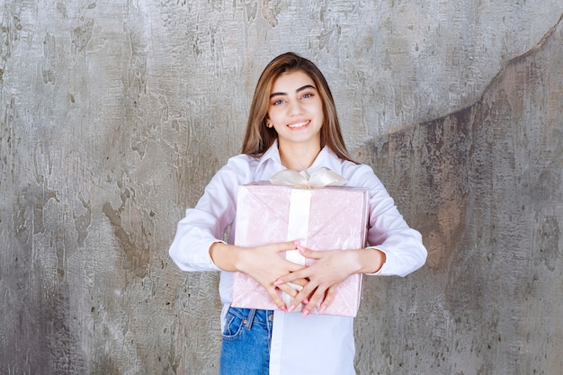 Fille en chemise blanche tenant une boîte-cadeau rose enveloppée d'un ruban blanc