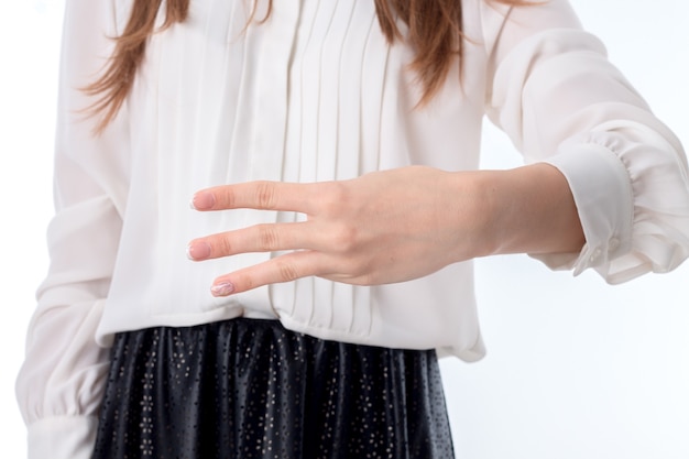 Fille en chemise blanche tendue la main et montre trois doigts sur le côté