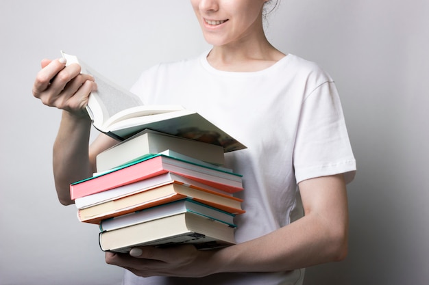 Fille en chemise blanche tient beaucoup de livres dans les mains. Lecture, tournage de page