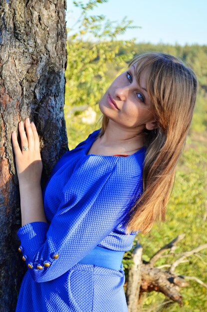 Une fille en chemise bleue se tient à côté d'un arbre